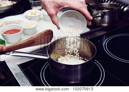 Chef is pouring rice in stewpan, toned image