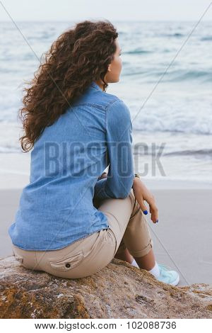 Beautiful Slim Woman With Curly Hair Sitting On A Rock By The Sea