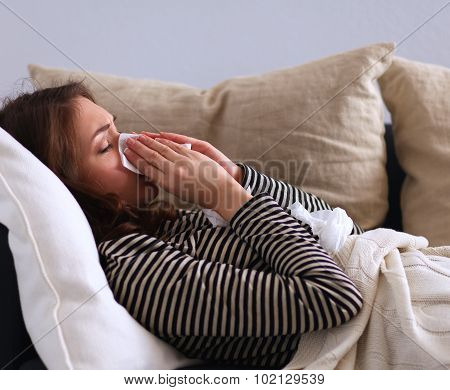 Portrait of a sick woman blowing her nose while sitting on the sofa
