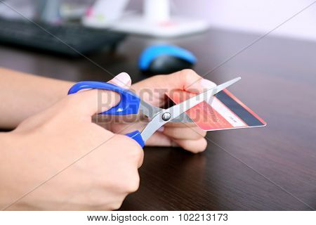 Woman's hands cutting bank card with scissors on wooden table background