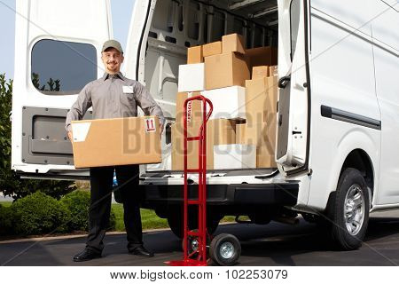 Young delivery man with parcel near cargo truck. Shipping service.