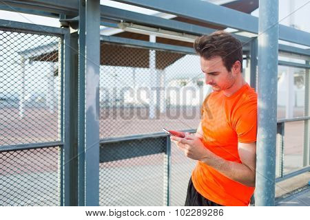 Men runner using cell telephone while relaxing after training outdoors in summer day