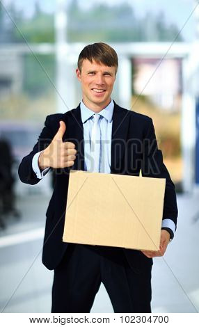 Smiling businessman holding a cardboard box and standing into an empty new office.