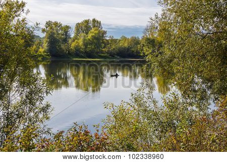 Autumn landscape with fisherman in a boat on the river