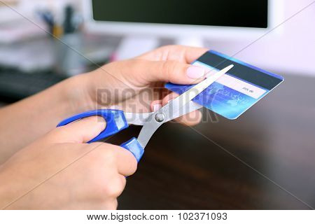 Woman's hands cutting bank card with scissors on wooden table background