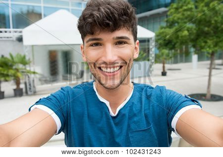Closeup shot of handsome young man take a selfie in the city center. Guy is photographing self outdoor. Shallow depth of field with focus on smiling young man taking selfie. 