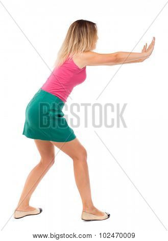 back view of woman pushes wall. Isolated over white background. Rear view people collection. backside view of person. Blond girl in a green skirt pushing something heavy right.