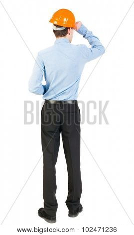 Backview of an engineer in construction helmet stands. Standing young guy. Rear view people collection.  The man in trousers and shirt standing at a construction site holding hand helmet.