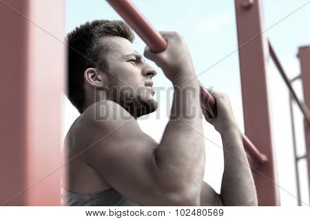 fitness, sport, exercising, training and lifestyle concept - young man doing pull ups on horizontal bar outdoors
