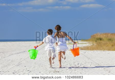 Happy children, boy girl, brother and sister running and having fun playing in the sand on a beach with bucket and spade
