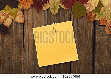 Orange adhesive note with a paperclip against autumn leaves on wood