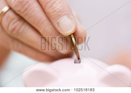 savings, money, annuity insurance, retirement and people concept - close up of senior woman hand putting coin into piggy bank
