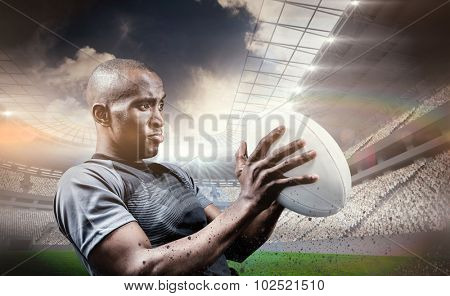 Rugby player looking away while throwing ball against rugby stadium