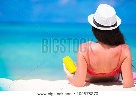 Beautiful young woman holding a suncream lying on tropical beach
