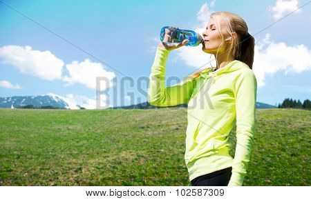 people, fitness, sport and healthy lifestyle concept - happy woman drinling water from bottle after workout over natural background