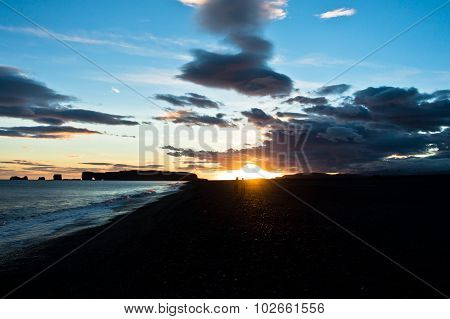 Sunset on black beach near Vik with Dyrholaey rock at background