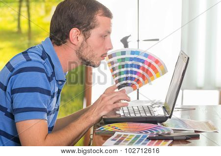 Man working on laptop while holding up palette, colormap from profile angle