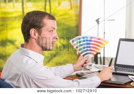 Man working on laptop while holding up palette, colormap from profile angle
