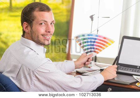 Man smiling to camera and working on laptop while holding up palette, colormap from profile angle
