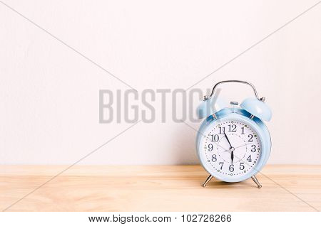 Light Blue Alarm Clock On Wooden Table And White Wall Background
