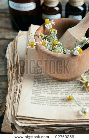 Old book with dry flowers in mortar and bottles on table close up