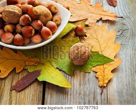 Bowl Of Nuts And Autumn Leaves On The Old Wooden Table