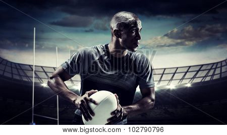 Determined rugby player holding ball against rugby stadium