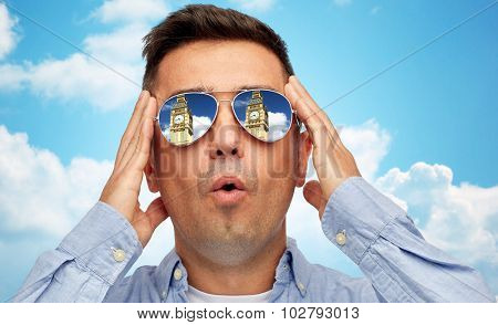 travel, tourism, sightseeing, emotions and people concept - face of man in sunglasses looking at big ben tower over blue sky and clouds background
