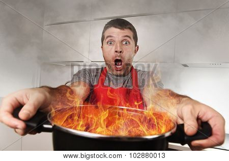 Inexperienced Home Cook With Apron Holding Pot Burning In Flames With Stress Panic Face Expression