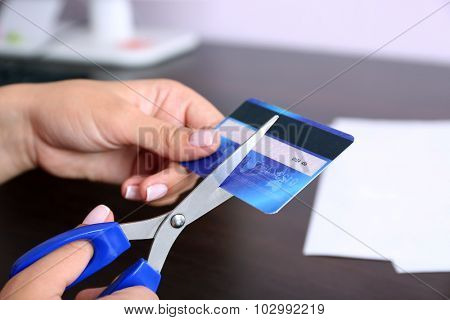 Woman's hands cutting bank card with scissors on wooden table background