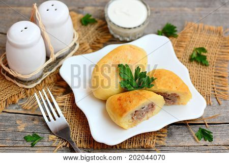 Homemade potato cutlets with mince meat filling on a white plate. Sour cream in glass bowl, fork, knife, burlap textile on an old wooden table. Rustic style