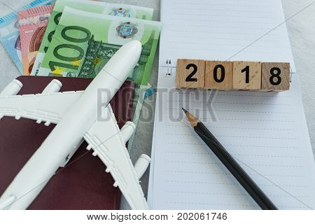 Travel planning target with toy airplane passport Euro banknotes with wooden block 2018 and pencil on paper note.