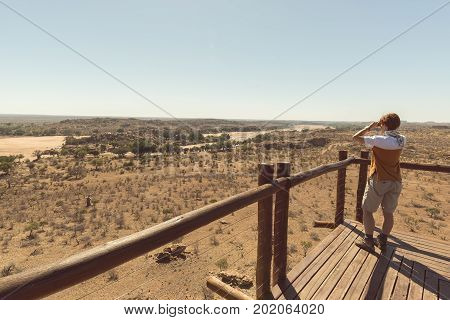 Tourist looking at panorama with binocular from viewpoint over the Mapungubwe National Park travel destination in South Africa.