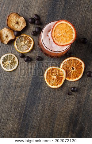Cocktail on rustic wood background. Cold citrus alcohol beverage with tequila, blood orange juice and ginger beer, served with ice, citrons and chocolate snacks, top view, copy space