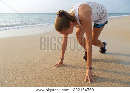 Female athlete in starting position ready for running. Young woman ready for sports exercise on beach