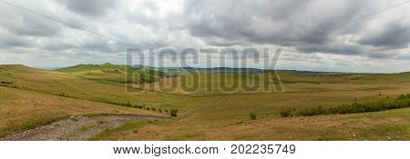 Dirt road through green hills against the sky with clouds