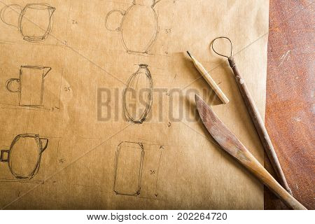 pottery manufacture artisan tools ceramics art concept - drawing of earthenware pencil and tools on the wooden table brown background top view