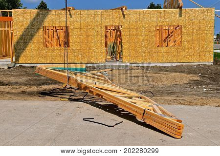 Pre-built rafters(trusses) are being lifted by a cable and boom to be placed on top of a wooden framed building under construction.