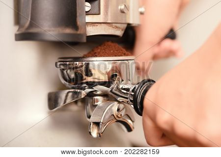 Barista holding portafilter with ground coffee from grinder prepare for making coffee from espresso machine