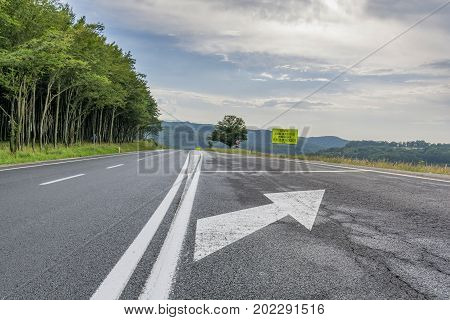 Highway passing near the beech forest in the evening. Asphalt road running near beech forest with road signs. English translation of Romanian road Caution dangerous curve ahead. Accident hazard 2 km.