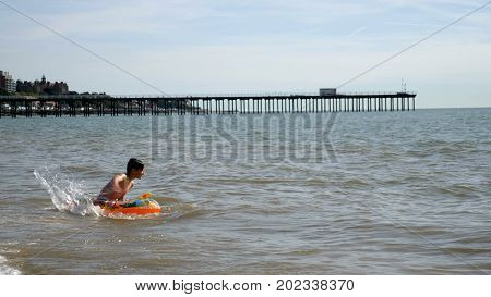 Teen Boy floats at British Seaside on Inflatable Mattress.