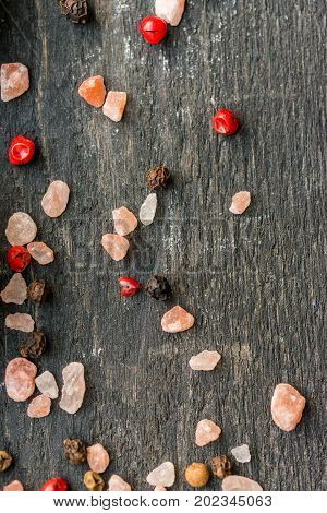 Close up grains of pink himalayan salt mixed with pink and red peppercorn on dark wooden surface