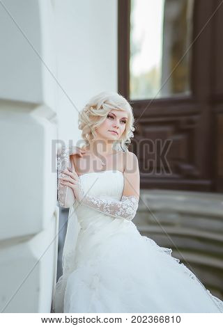 Blonde bride with a thoughtful look with a bouquet on a light background.