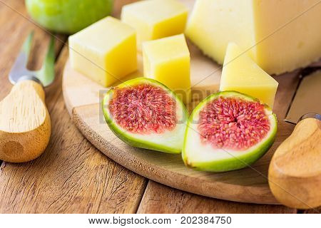Wedge of Spanish cured hard goat cow ewe cheese cut in cubes on wood platter. Ripe halved green figs with red pulp. Knife and fork. Traditional appetizer tapas mediterranean cuisine.