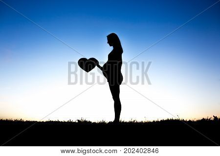 A Pregnant woman touch her belly sit on the ground against the light