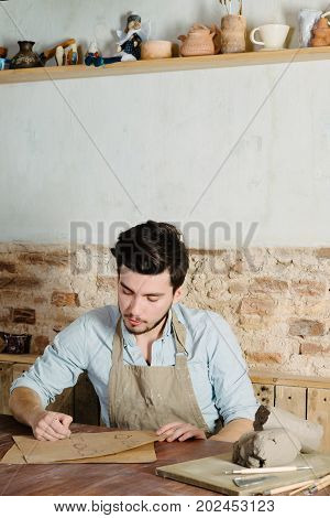 handsome young mexican potter does sketches of ceramics on the paper. concept of small business handcrafted hobby work.