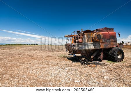 Old burned agriculture combines in a flattened grainfield under a blue sky with white clouds in the countryside of france