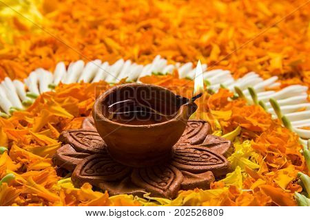 flower rangoli for Diwali or pongal or onam made using marigold or zendu flowers and red rose petals over white background with diwali diya in the middle, selective focus