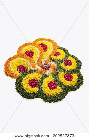 flower rangoli for Diwali or pongal or onam made using marigold or zendu flowers and red rose petals over white background with diwali diya in the middle, selective focus