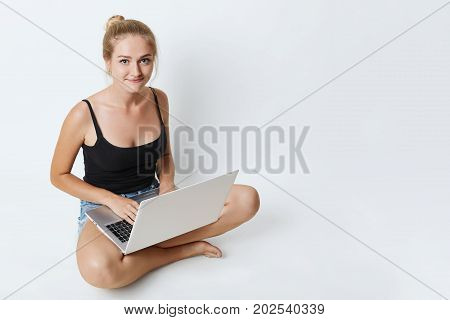 Cute Female Sitting On Floor With Crossed Legs, Using Laptop Computer For Searching Information Or E